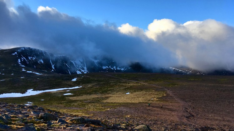 Clouds flowing over mountains with blue skies above and bright foreground of rocks