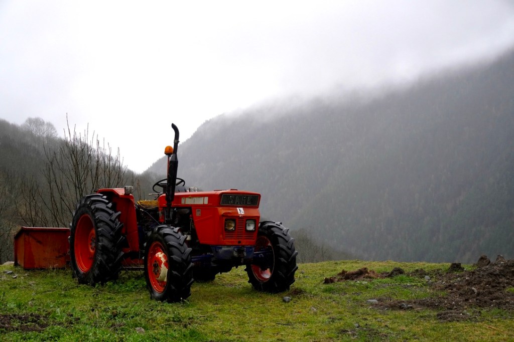 Photo of a red tractor in the foreground with misty mountains behind